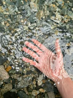 a person's hand is in the water with rocks and stones around them,