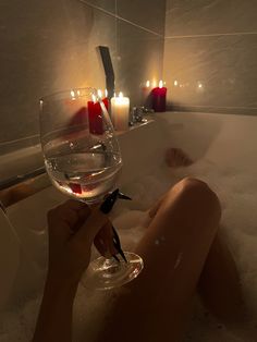 a person holding a wine glass in a bathtub with candles on the wall behind them