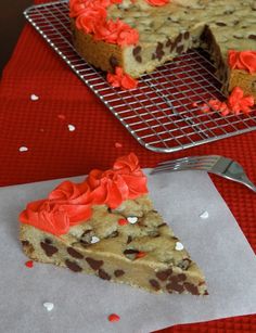 a slice of cookie cake with red icing on a plate next to a cooling rack