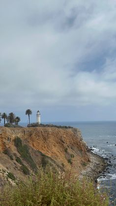 a lighthouse on top of a cliff by the ocean with palm trees in the foreground