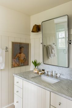 a bathroom with marble counter tops and white cabinets, along with a large mirror above the sink