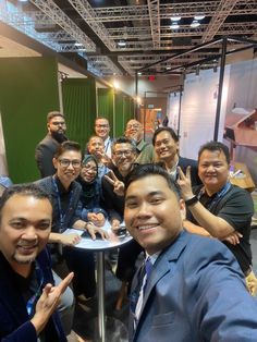 a group of people sitting around a table posing for the camera with their thumbs up