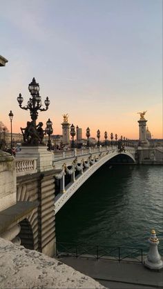 a bridge that is over some water and has statues on the side of it at sunset