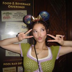 a young woman making the peace sign with her hands in front of her head and wearing mickey ears