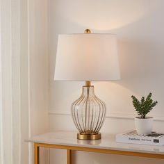 a table with a lamp on it next to a book and a potted plant