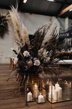 some white candles are sitting on a table with dried flowers and pamodia in them