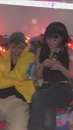 two people sitting on a couch with one holding a bottle and the other looking at his cell phone