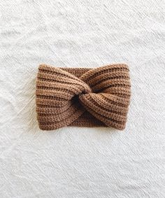 a brown knitted headband laying on top of a white blanket with a knot in the middle