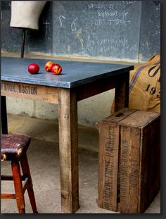 an old wooden table with apples on top and two stools next to it in front of a chalkboard wall