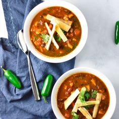 two bowls of chili and tofu soup on a blue towel with green peppers next to it