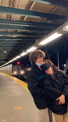 a man and woman standing next to each other at a train station while talking on their cell phones