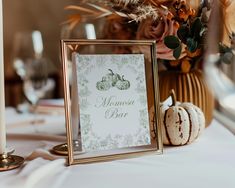 a table topped with a framed sign next to a vase filled with flowers and pumpkins