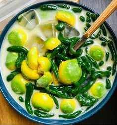 a blue bowl filled with green vegetables and white sauce on top of a wooden table