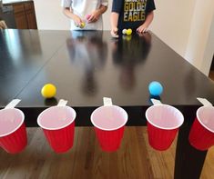 two children playing with plastic cups and balls on a table in the middle of a room