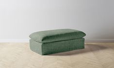 a green ottoman sitting on top of a hard wood floor next to a white wall