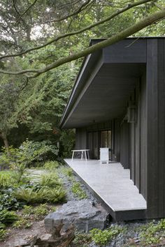 the house is surrounded by trees and rocks, with an outdoor seating area on one side