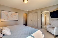 a bedroom with a bed, chair and flat screen tv mounted on the wall above it