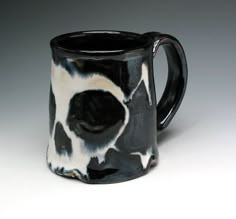 a black and white coffee mug with a skull design on it's side, in front of a gray background