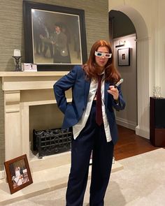 a woman in a suit and tie standing in front of a fire place with her hands on her hips