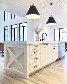 a kitchen with white cabinets and black pendant lights over the island in front of two windows