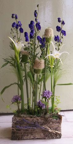 an arrangement of blue and white flowers in a wood block planter on the floor