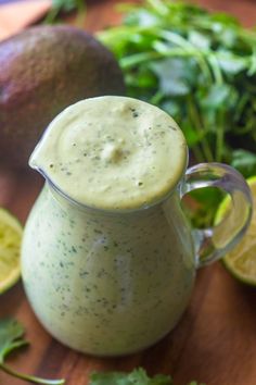 a pitcher filled with green liquid next to sliced limes and avocado on a cutting board