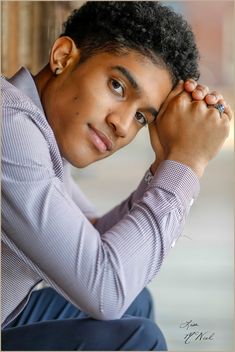 a young man with his hand on his head and looking at the camera while sitting down