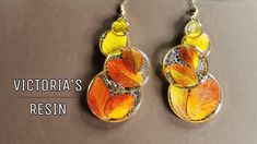 a pair of yellow and orange leaves are hanging from silver earwires with the words victoria's resin