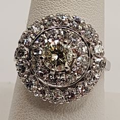 a diamond ring is sitting on top of a white cloth covered stand, with the center stone surrounded by smaller round diamonds