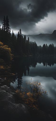 a lake surrounded by trees under a cloudy sky with dark clouds above it and mountains in the distance