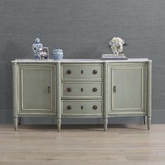 an antique sideboard with drawers and vases on top, against a gray wall