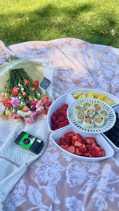 fruit and flowers are arranged in bowls on a picnic blanket with a cell phone next to it