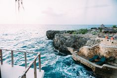 people are standing on the edge of a cliff by the ocean