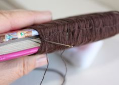 a person is holding a piece of brown yarn and some sewing needles in their hand