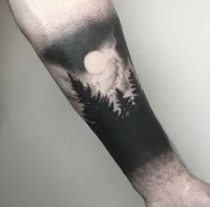 a person with a black and white tattoo on their arm that has trees in the background