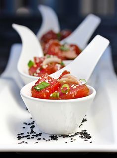 two white bowls filled with food on top of a table covered in black seeds and garnishes