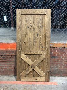 a wooden door sitting on the side of a road next to a brick wall and fence