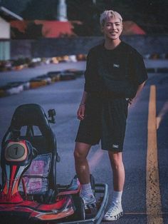 a young man standing next to a go kart on the street with his hands in his pockets