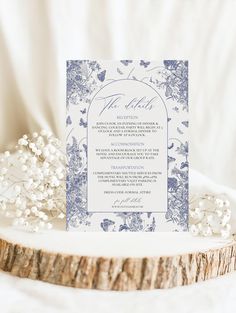 a white and blue wedding card on top of a piece of wood with baby's breath