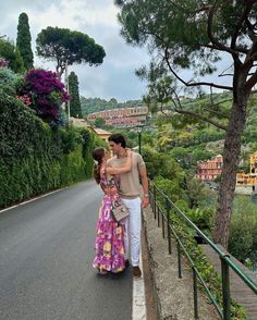 a man and woman walking down the road with trees on both sides, in front of them