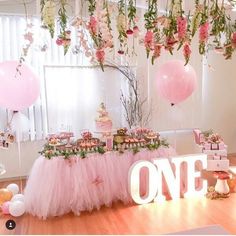 a table topped with lots of pink and white balloons next to a sign that says one