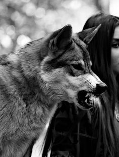 a woman is standing next to a wolf