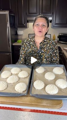 a woman holding two trays of pastries on top of a kitchen counter next to an oven