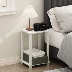 an alarm clock sitting on top of a white table next to a lamp and bed