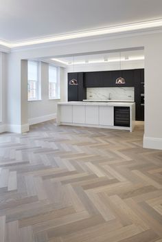 an empty living room and kitchen area with wood flooring in the foreground, large windows to the right