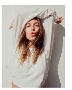 a woman with her eyes closed standing in front of a white wall and covering her face