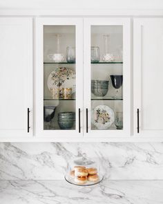 a kitchen with marble counter tops and white cupboards filled with plates and bowls on top of them