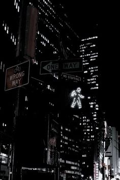 street signs in the city at night with lights and skyscrapers lit up behind them