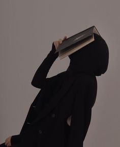 a person sitting in a chair with a book on their head and holding it up to their face