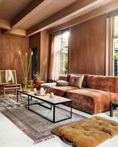 a living room filled with lots of furniture next to a large window and wooden paneled walls